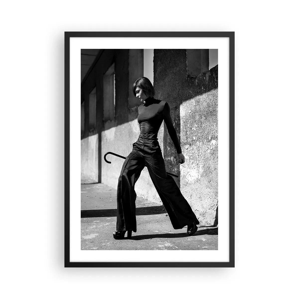 Plakat w czarnej ramie - Kobieta w eleganckim stroju z laską na tle surowej architektury - 50x70cm - Miejska elegancja - Nowoczesna dekoracja ścienna do salonu i sypialni ARTTOR