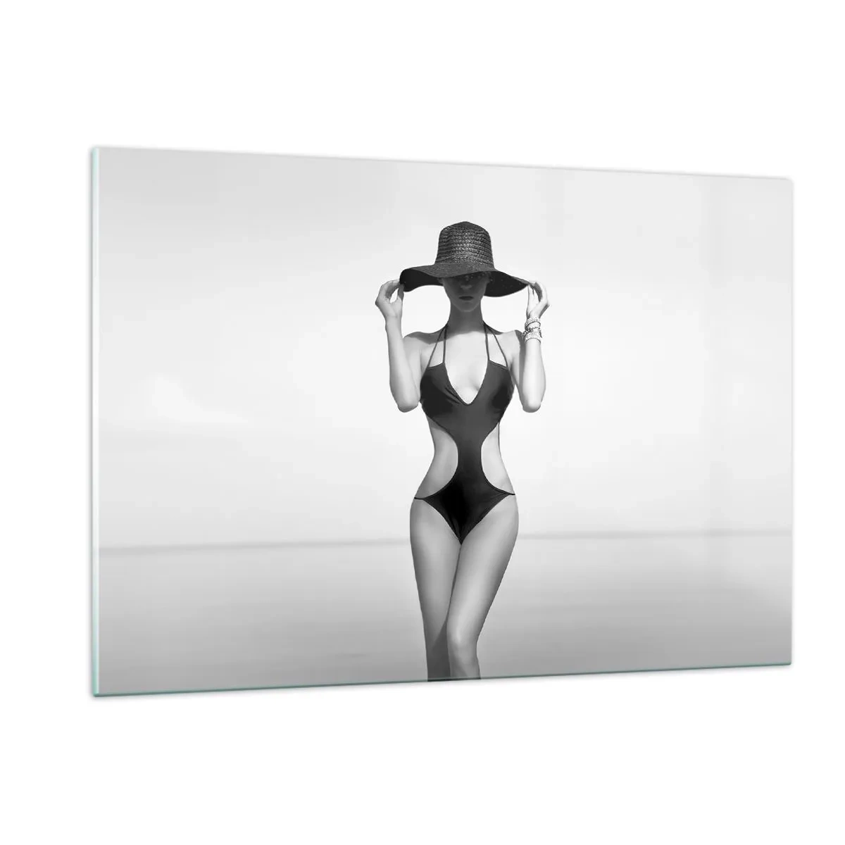 Obraz na szkle - Kobieta w czarnym stroju kąpielowym i kapeluszu na tle morza - 120x80cm - Na imię mi: Elegancja - Nowoczesna dekoracja ścienna do salonu, kuchni i sypialni ARTTOR