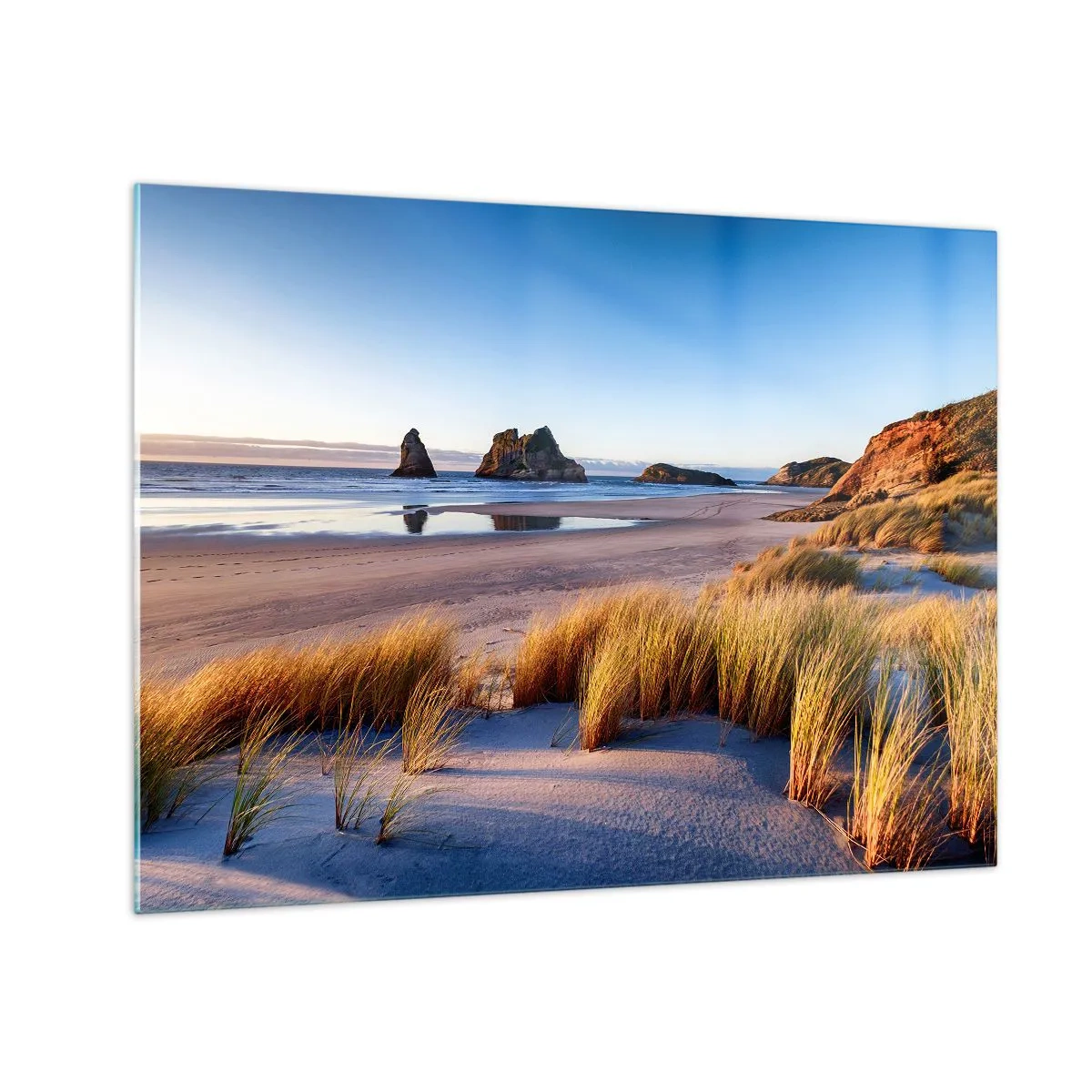 Obraz na szkle - Plaża o świcie z trawami i skałami w tle przy spokojnym morzu - 70x50cm - Dla poszukiwaczy spokoju - Nowoczesna dekoracja ścienna do salonu i sypialni ARTTOR