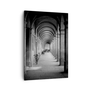 Obraz na płótnie - Czarno-biała fotografia długiego korytarza z arkadami i zaparkowanymi rowerami - 50x70cm - Pod arkadami - Nowoczesna dekoracja ścienna do salonu, kuchni i sypialni ARTTOR
