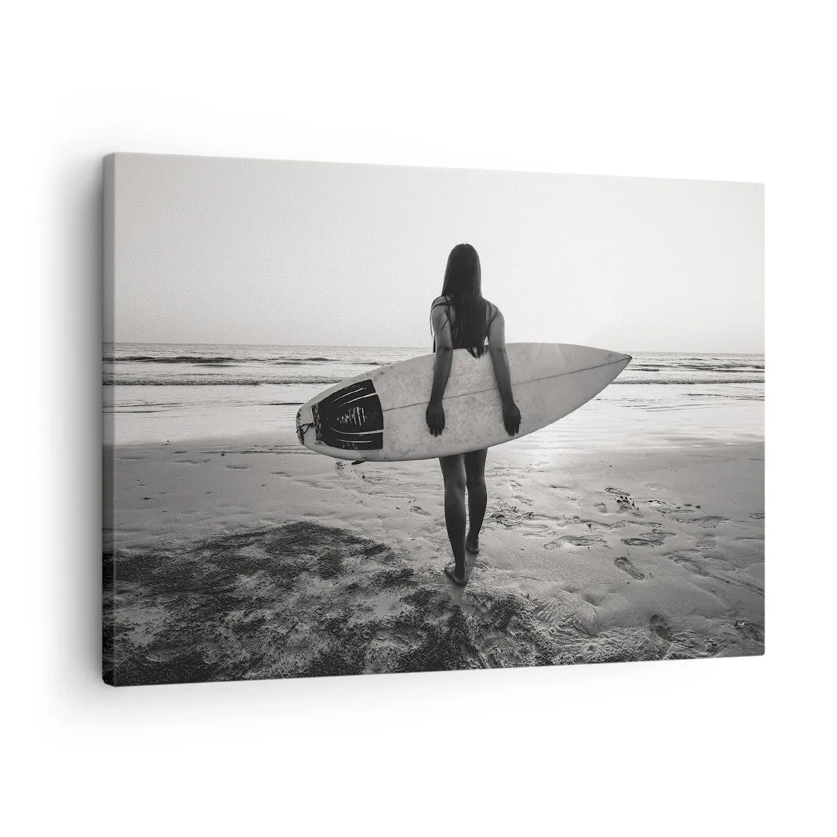 Obraz na płótnie - Kobieta z deską surfingową na plaży w czerni i bieli - 70x50cm - Córka morskiej fali - Nowoczesna dekoracja ścienna do salonu i sypialni ARTTOR