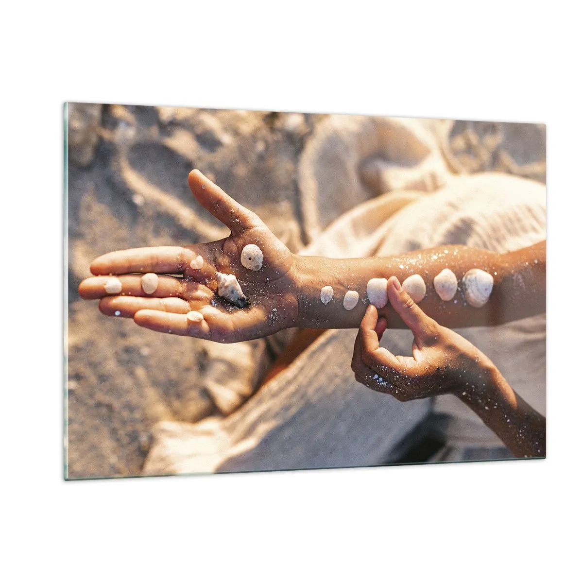 Obraz na szkle - Dłonie dziecka z muszelkami na tle piasku i tkaniny - 120x80cm - Piękno w zasięgu ręki - Nowoczesna dekoracja ścienna do salonu, kuchni i sypialni ARTTOR